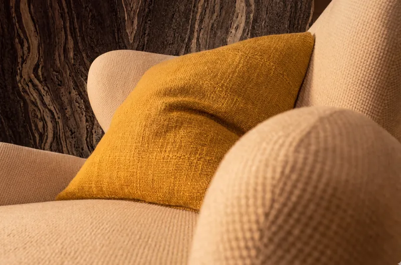 Detalle de sillón tapizado en tejido con cojín mostaza